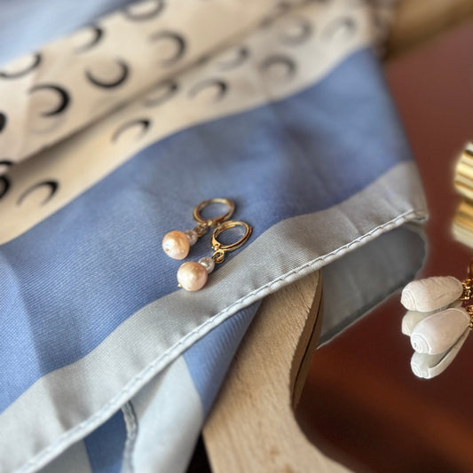 Gold and silver earrings on a patterned fabric with a bottle in the background