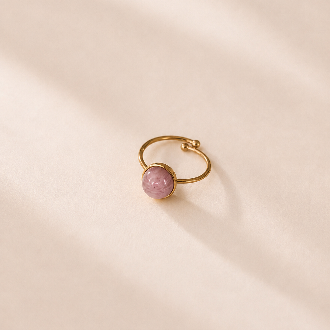 Gold ring with a pink gemstone on a beige background