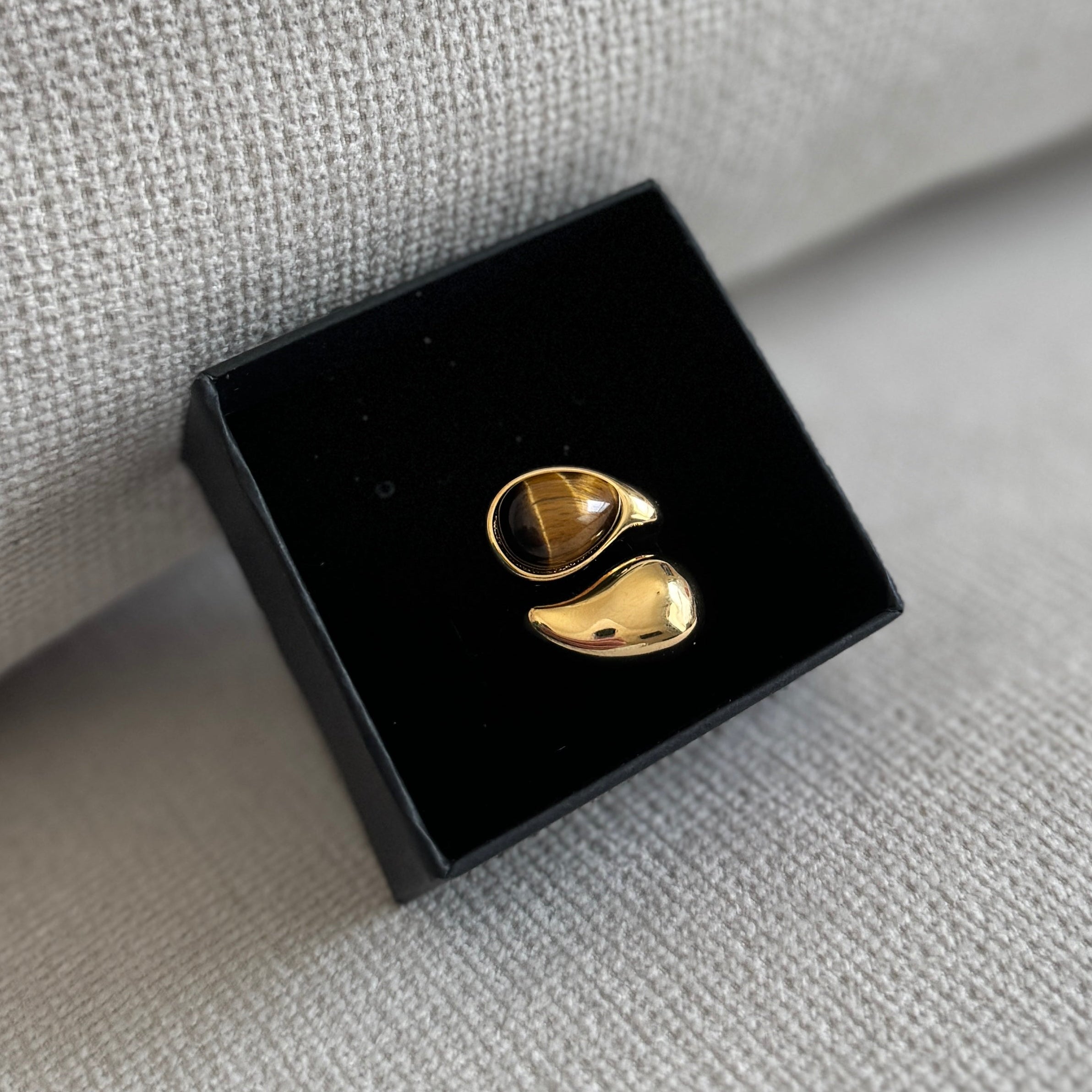 Gold earrings on a black display stand against a textured gray background
