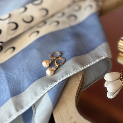 Gold and silver earrings on a patterned fabric with a bottle in the background