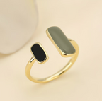 Gold ring with black and green stones on a beige background
