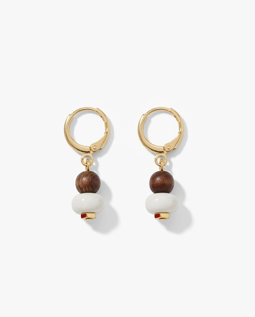 A pair of gold hoop drop earrings featuring a small dark brown wooden bead, a larger white spherical bead, and a tiny red accent bead at the bottom, displayed on a clean white background.