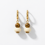 Pair of gold earrings with white beads on a light gray background